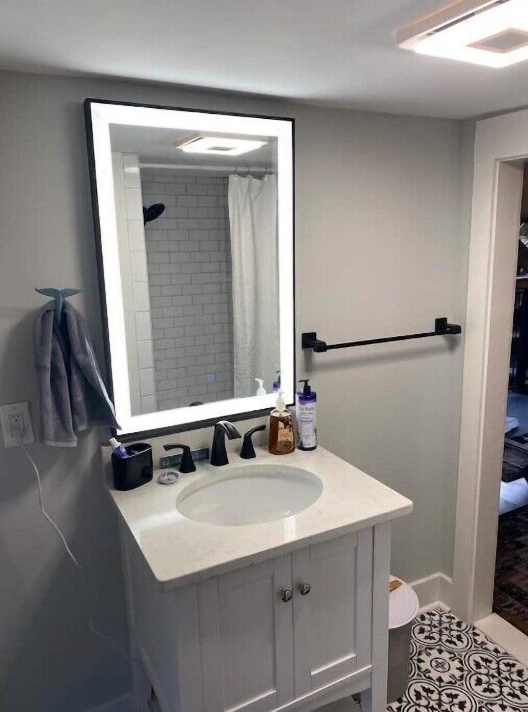 Een badkamer met een wit wastafelmeubel, een spiegel met verlichting, een handdoekhouder en een toilet.