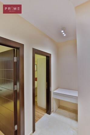 A hallway with a wooden door, a white shelf, and a ceiling light.