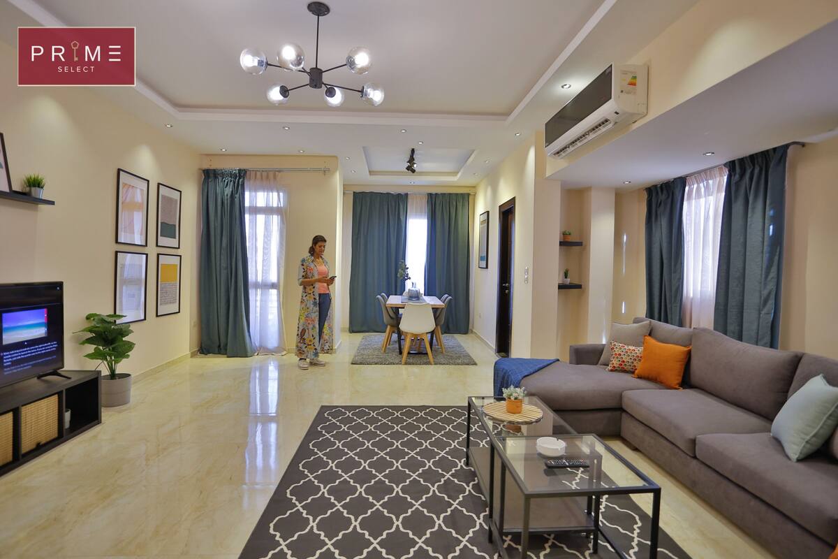 Uma sala de estar moderna com televisão de tela plana, um sofá, uma mesa de centro e um espaço de jantar com mesa e cadeiras.