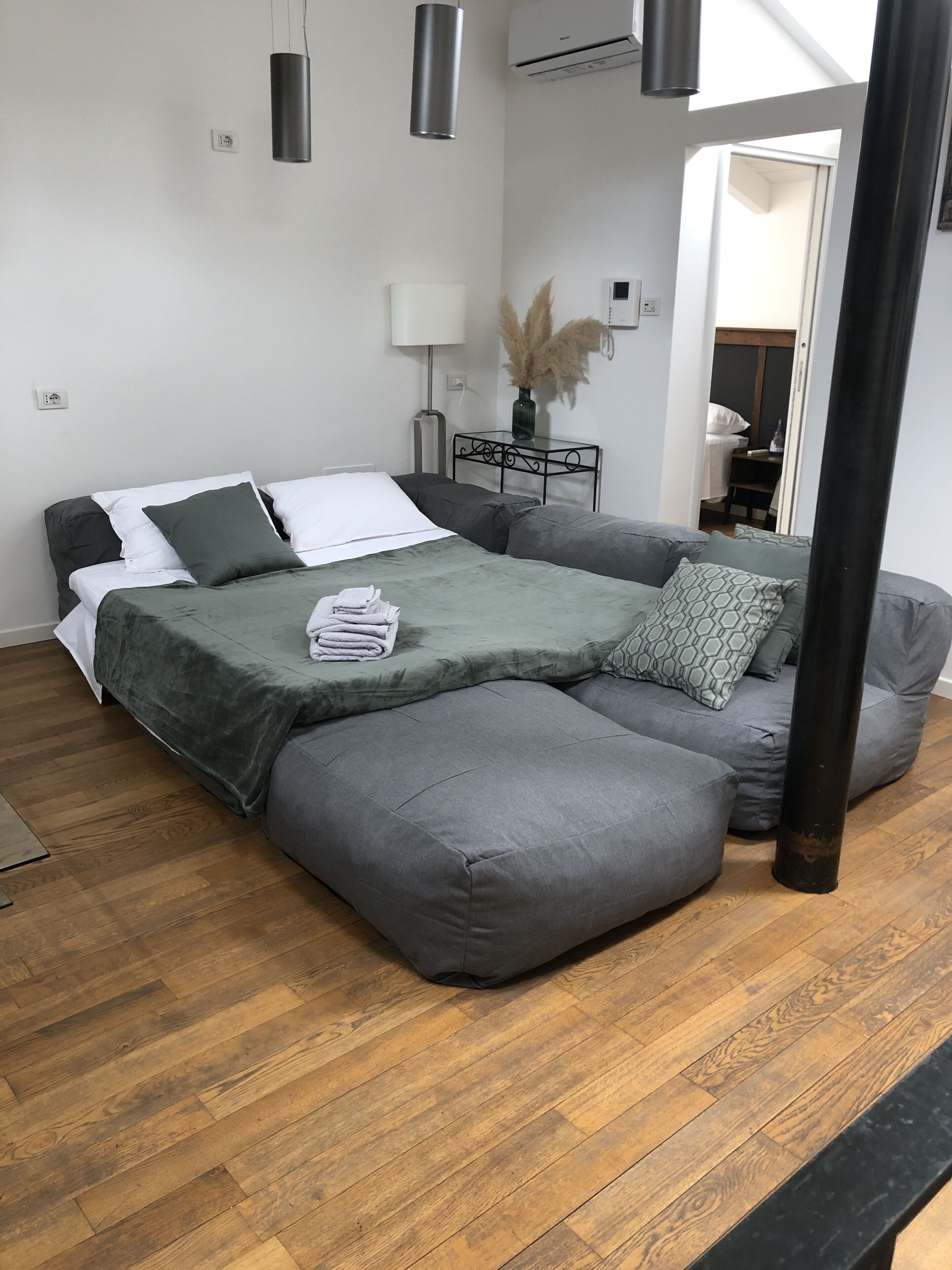 A modern bedroom with a bed, grey sofa, and a wooden floor.