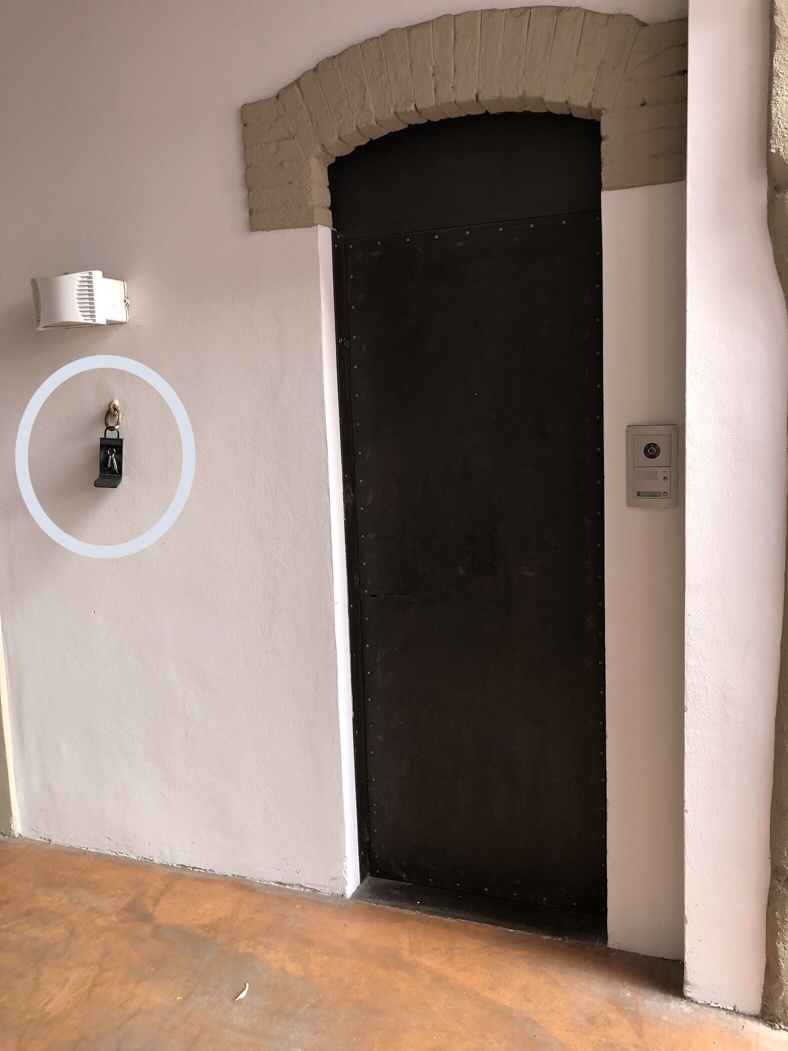A room with a dark door, a white wall, and a small circular window.