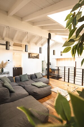Ein modernes Wohnzimmer mit einer Eckcouch, einem Glastisch und Blick auf die Küche und den Balkon.