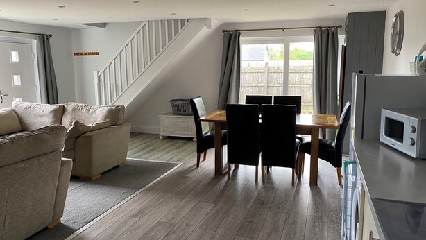 A modern living room with a sofa, dining table, chairs, a staircase, and a kitchen area with a microwave. - Cosy Cotswold Coachhouse - Rural and quiet (Chalford)