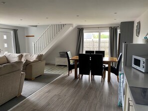 A modern living room with a sofa, dining table, chairs, a staircase, and a kitchen area with a microwave.
