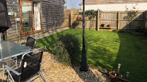 A backyard with a wooden fence, a lawn, a table with chairs, and a street lamp. - Cosy Cotswold Coachhouse - Rural and quiet (Chalford)