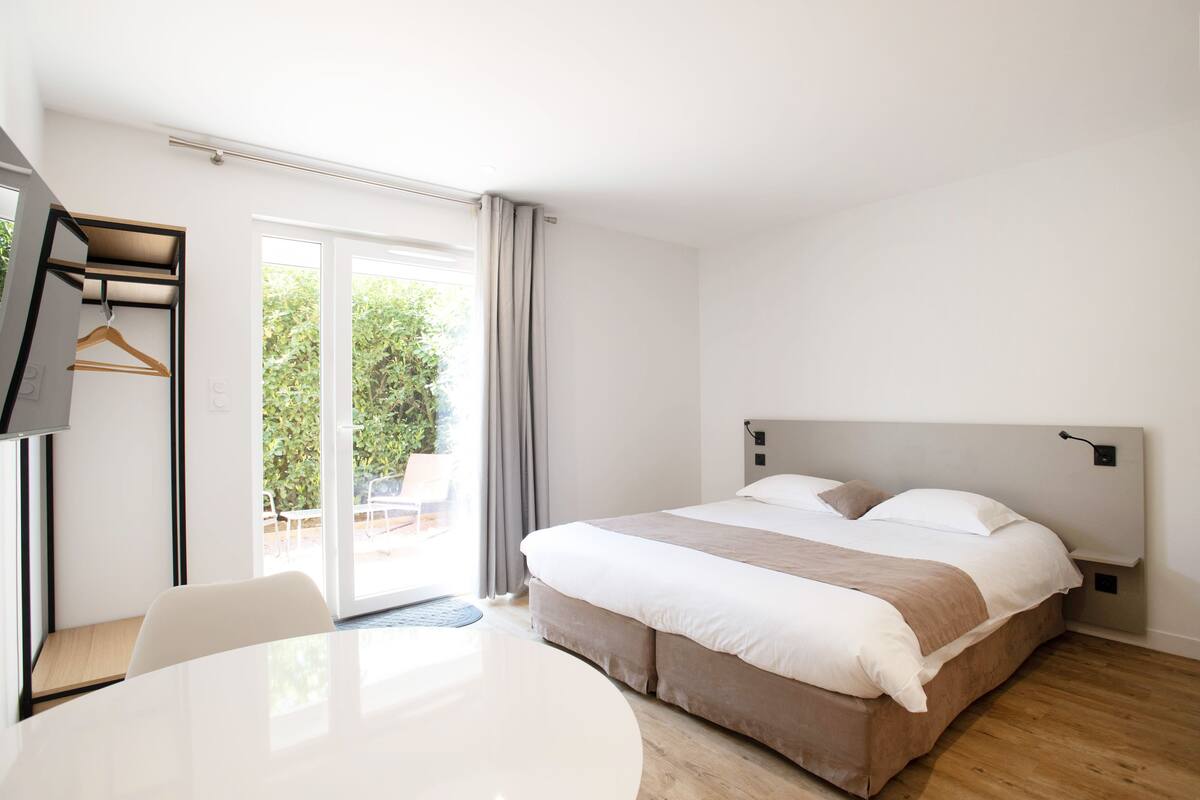 A modern hotel room with a large bed, a desk, and a view of the outdoors.