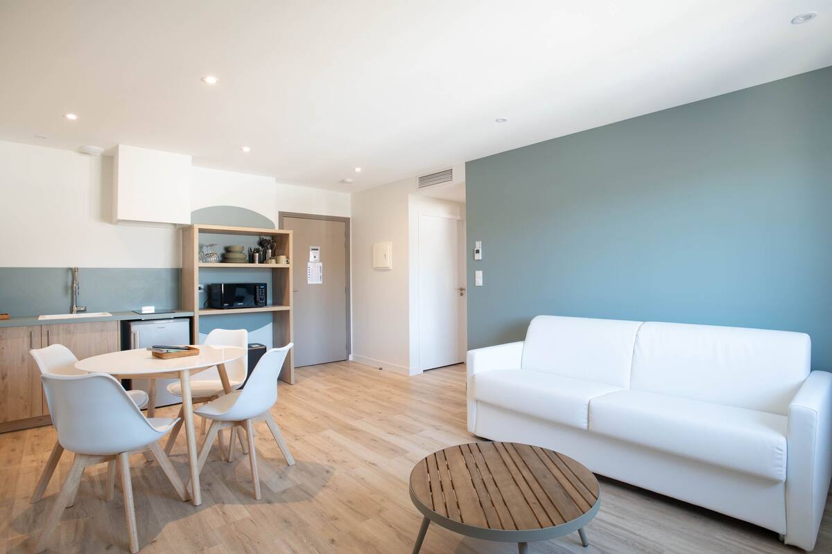 A modern living room with a white sofa, a round wooden coffee table, and a dining area with a white table and chairs.