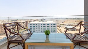 Ein Balkon mit zwei Korbstühlen, einem Glastisch und einem Blumentopf.