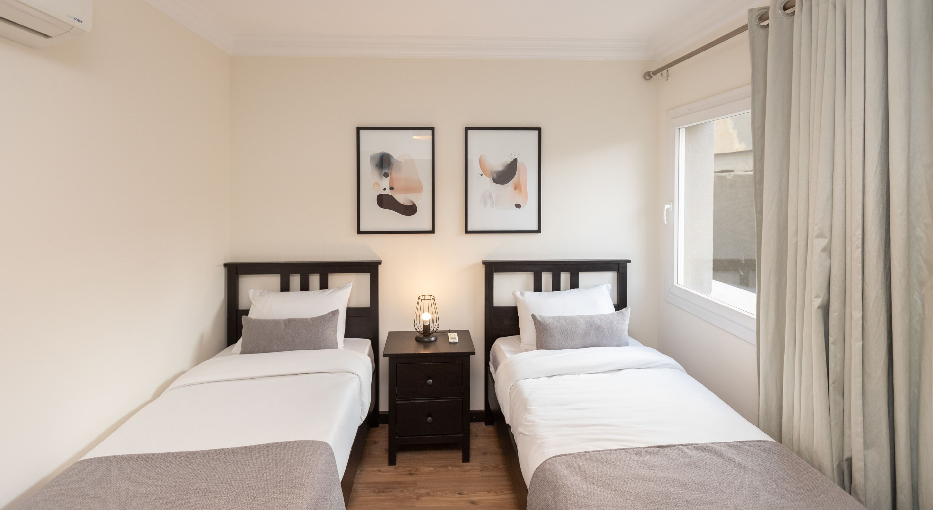 A double room with two beds, a nightstand with a lamp, and two framed artworks on the wall.