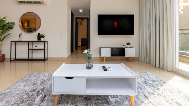 Ein modernes Wohnzimmer mit weißem Couchtisch, Wandfernseher, Topfpflanze und einer Ablagetisch.