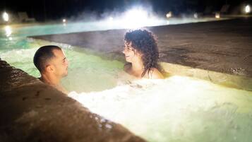 A couple in a hot tub at night with a pool in the background.