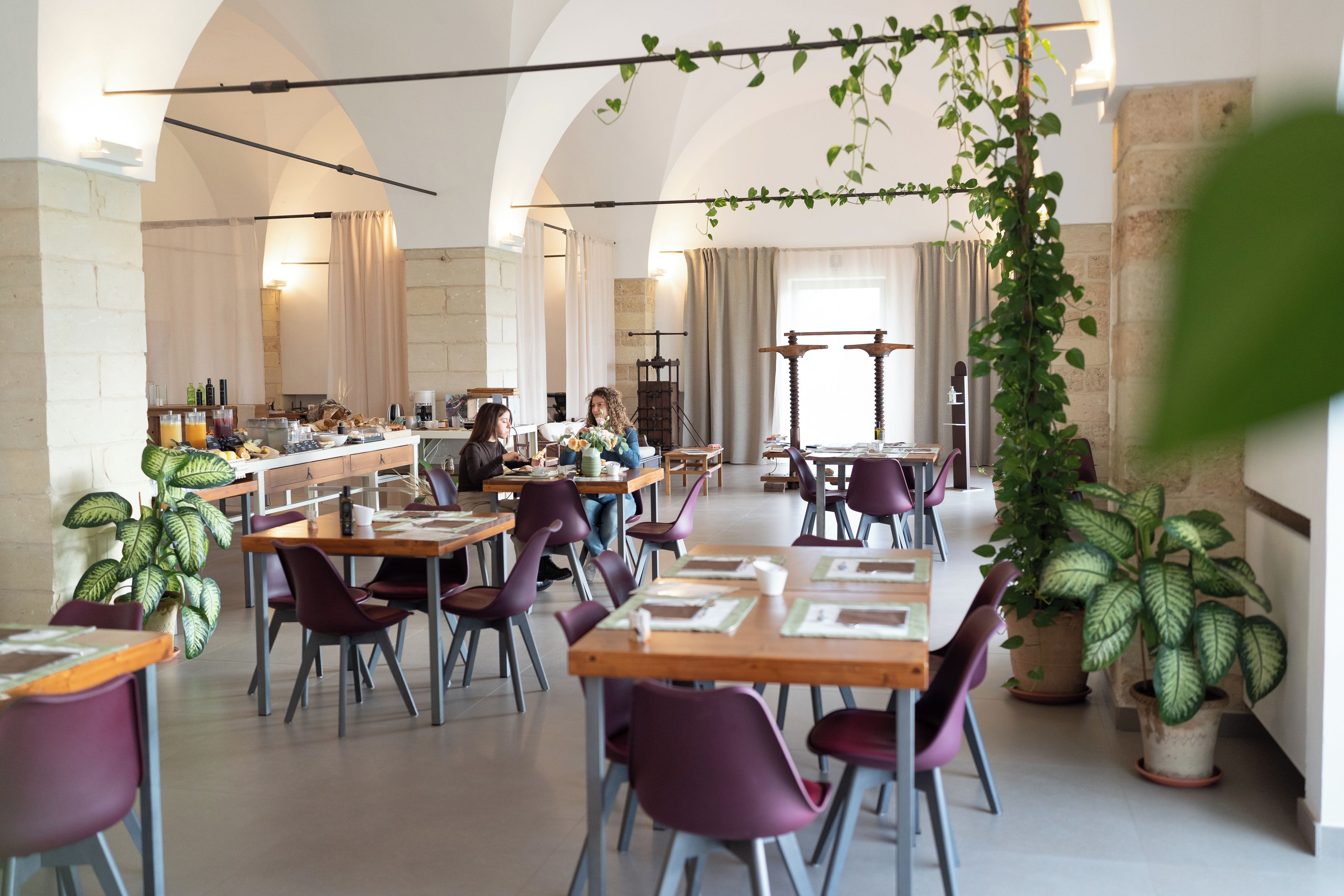 A spacious dining area with multiple tables and chairs, a bar area with beverages, and potted plants.