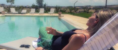 A person reclining on a lounge chair by a pool with a clear view of the surrounding landscape.