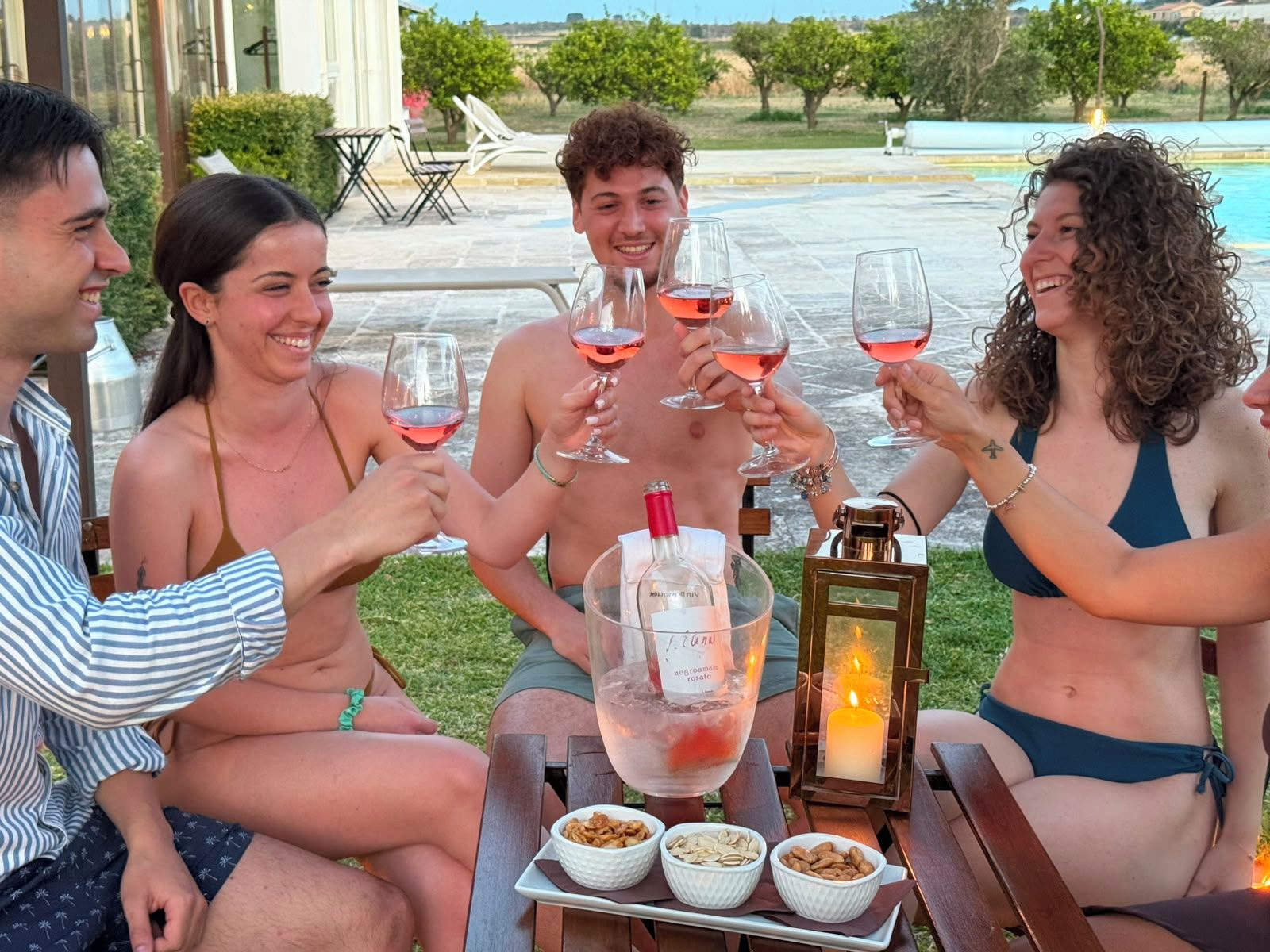 A group of people toasting with wine glasses at an outdoor table with a candle and snacks.