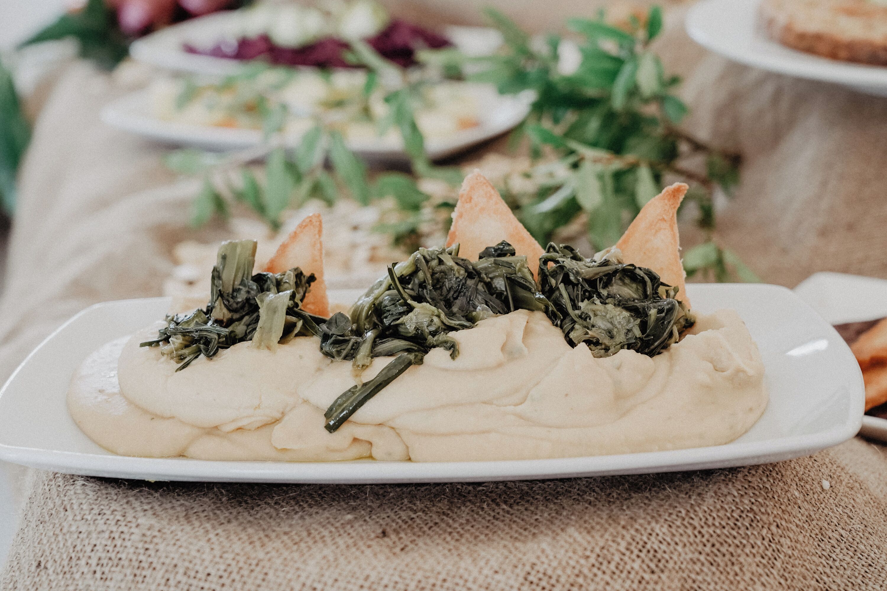 Une assiette de nourriture comprenant des légumes verts et une base blanche, peut-être un plat à base d’épinards et d’une sauce crémeuse, le tout servi dans une assiette blanche.