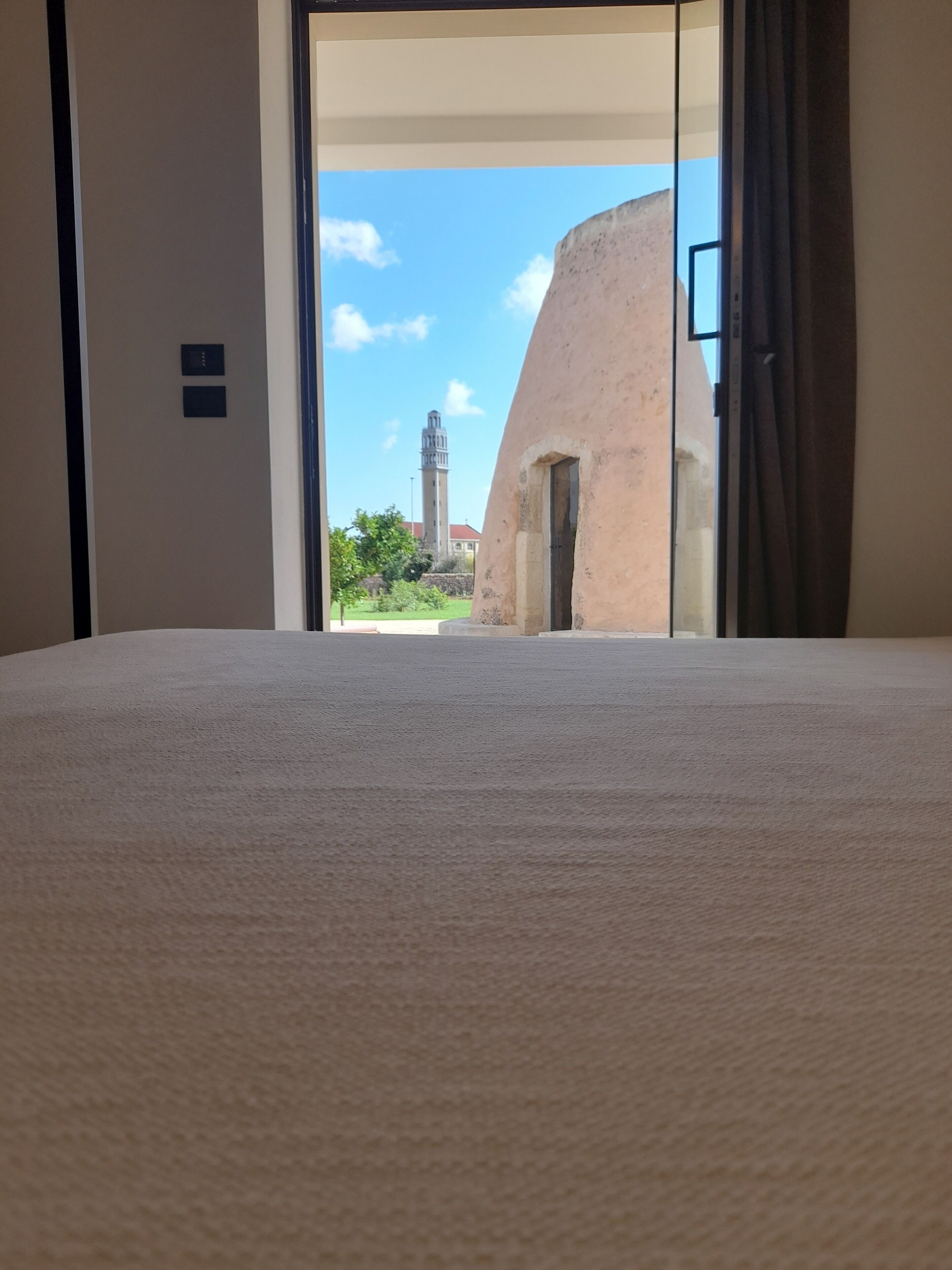 A hotel room with a large bed, a sliding glass door leading to a courtyard with a building and a tower in the background.