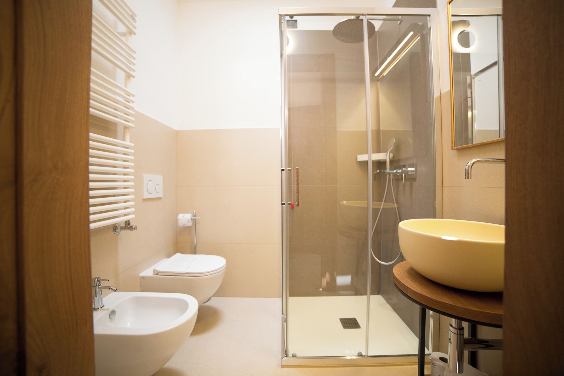 Een moderne badkamer met een douchecabine van glas, een wit toilet, een bidet en een rond wastafeltje op een houten aanrecht.