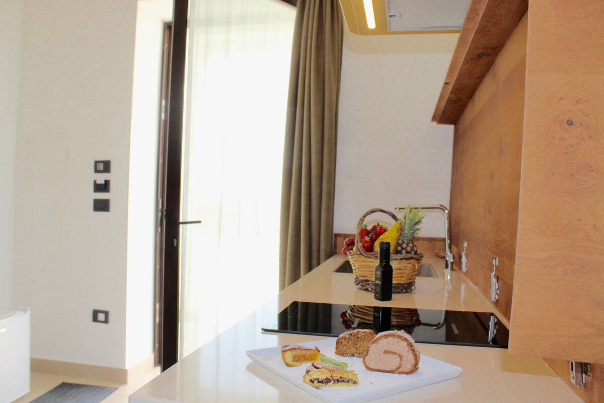 A kitchen counter with a cutting board, a loaf of bread, and a basket of fruit.