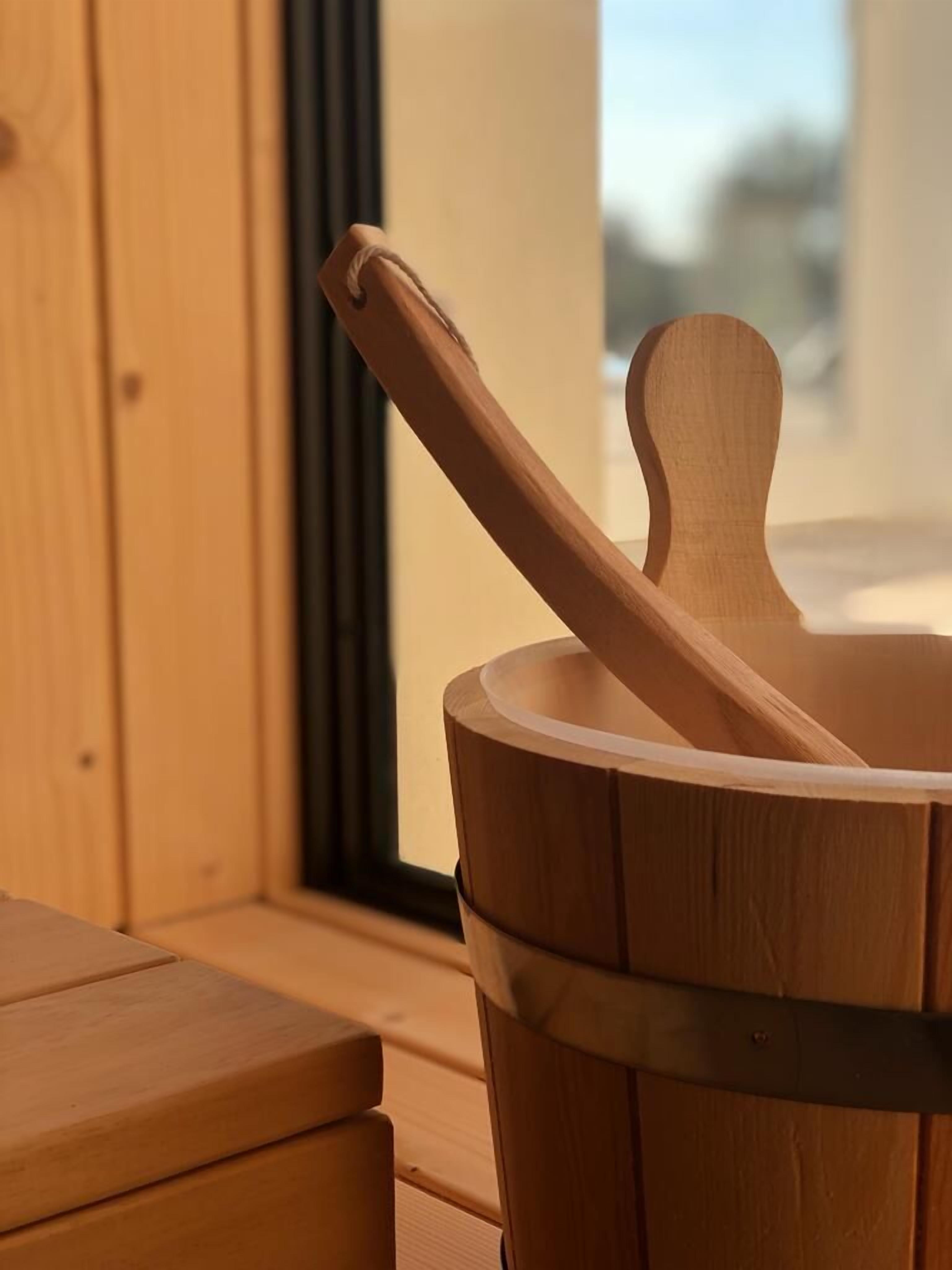 A wooden bucket with a wooden spoon inside, placed on a wooden surface near a window.