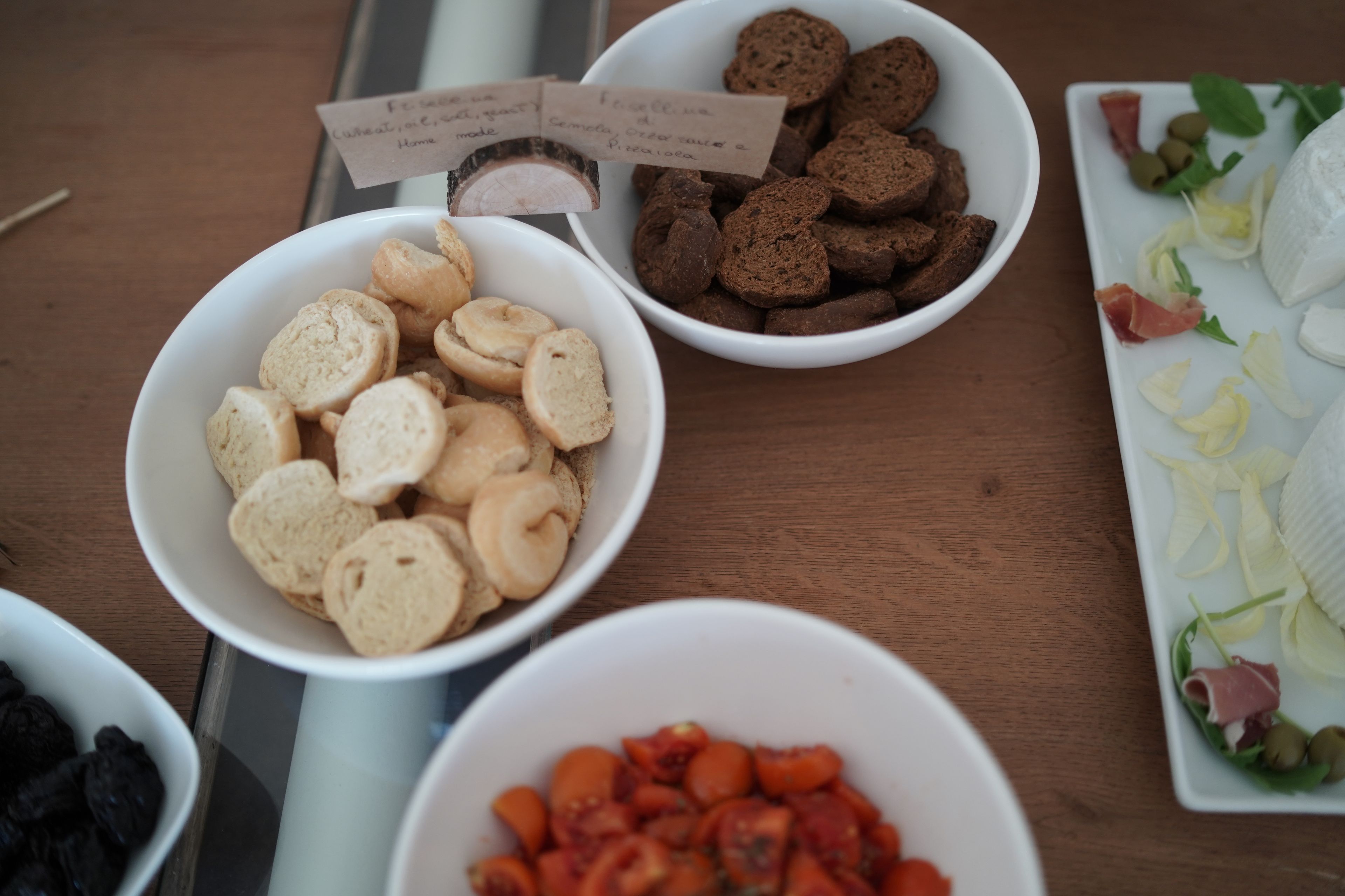 Una mesa con diferentes alimentos en cuencos, incluyendo pan en rodajas, galletas de color café oscuro y tomates.