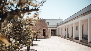 A courtyard with a modern building, a tree, and a brick structure. - Masseria Rifisa AgriResort (Caprarica di Lecce)