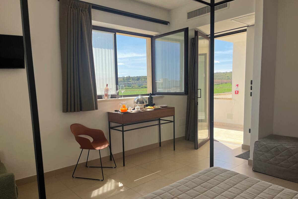 A room with a bed, a desk with breakfast items, a chair, and a view of the outdoors.