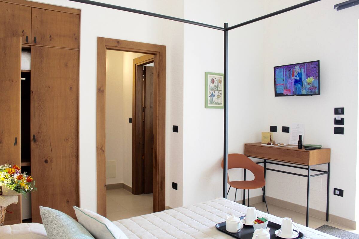 A modern hotel room with a bed, a desk, a chair, and a TV.