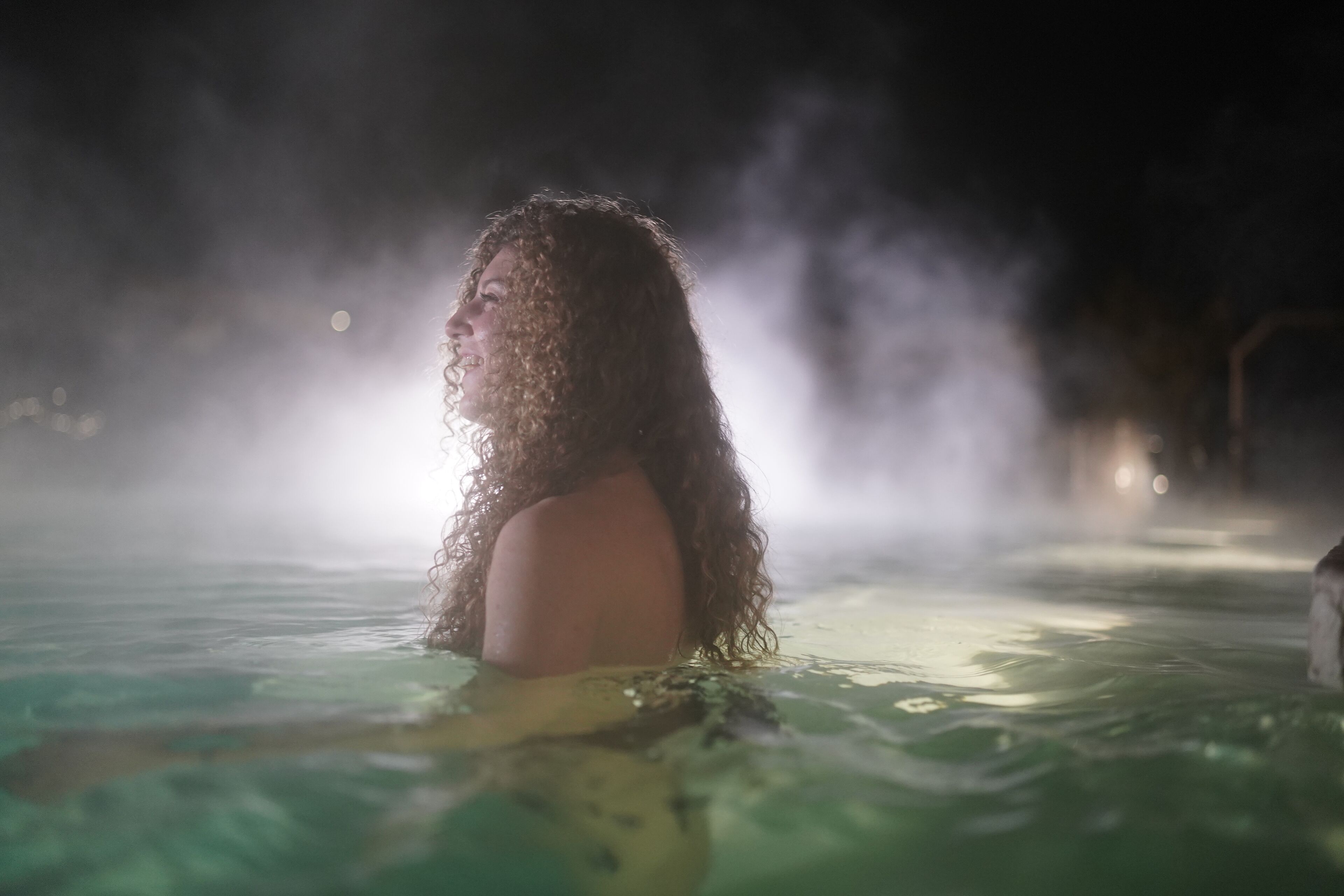 A person in a hot spring with steam rising, surrounded by mist.