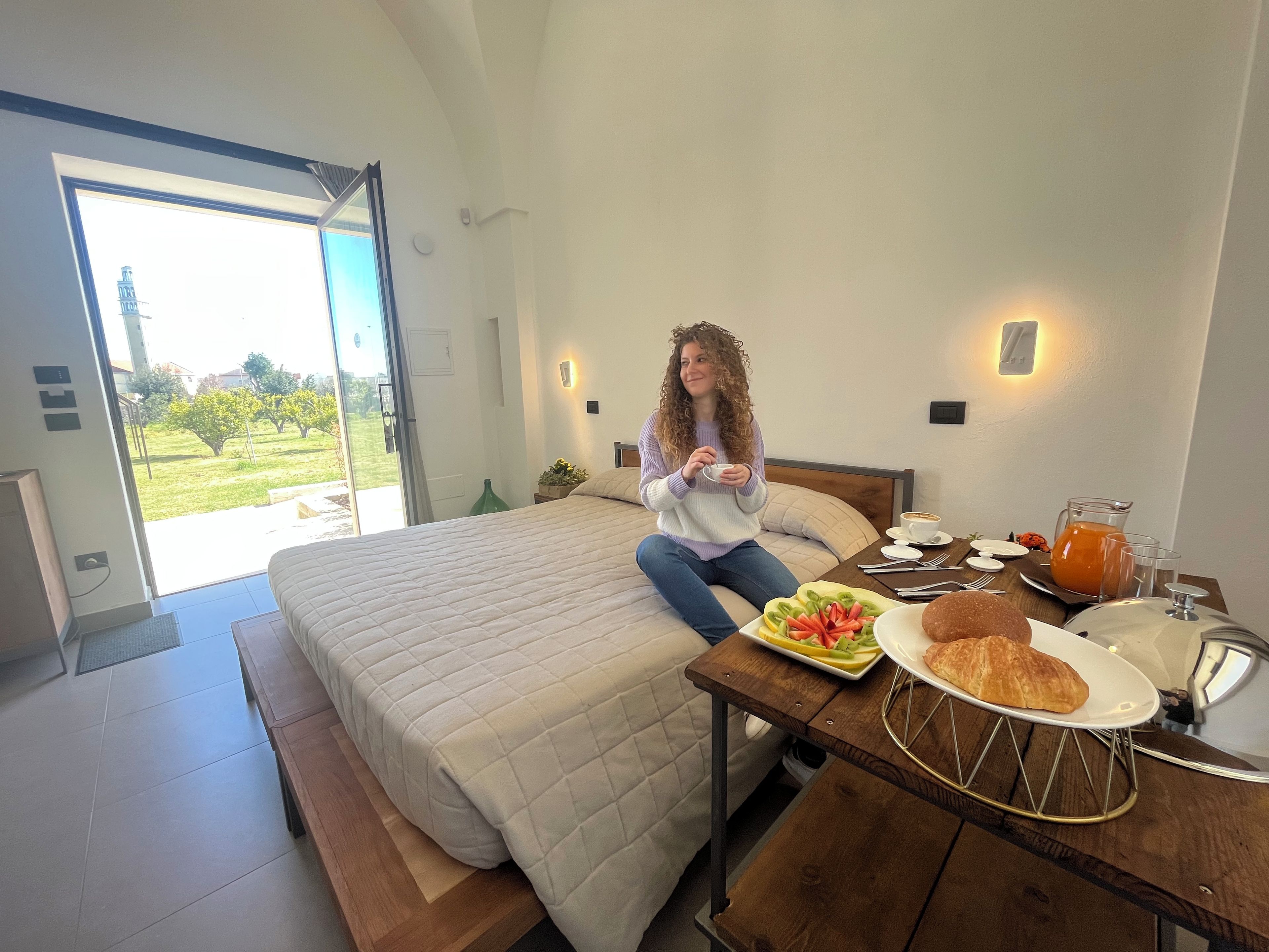 Un dormitorio con cama, una mesa de desayuno con comida y bebidas, y vistas al exterior.