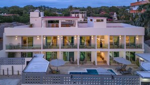 A modern multi-story hotel with a pool area, outdoor seating, and a view of the surrounding landscape. - Petras (Puerto Escondido)