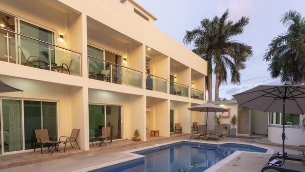 A modern hotel with a pool, outdoor seating, and palm trees. - Petras (Puerto Escondido)