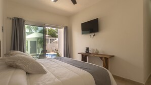A bedroom with a bed, a flat-screen TV, a coffee maker, and a view of an outdoor area with a pool and umbrellas. - Petras (Puerto Escondido)