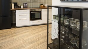 A modern kitchen with a black refrigerator, white cabinets, a glass cabinet with plates and wine glasses, and a 'MILK HOUSE' sign on the wall. - Wohnen im Milchhäusle von Schnait (Weinstadt)
