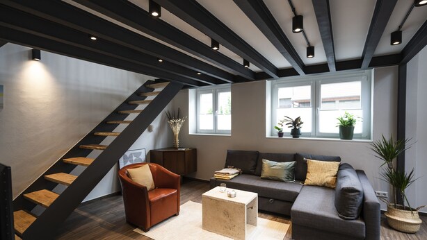 A modern living room with a staircase, a sofa, a coffee table, and a potted plant. - Wohnen im Milchhäusle von Schnait (Weinstadt)