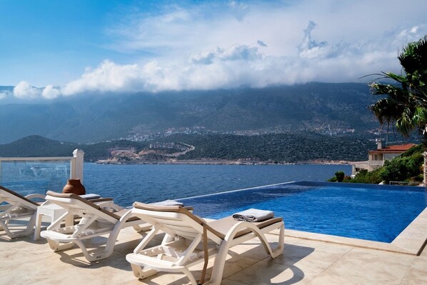 A poolside area with lounge chairs and a view of the sea and mountains.