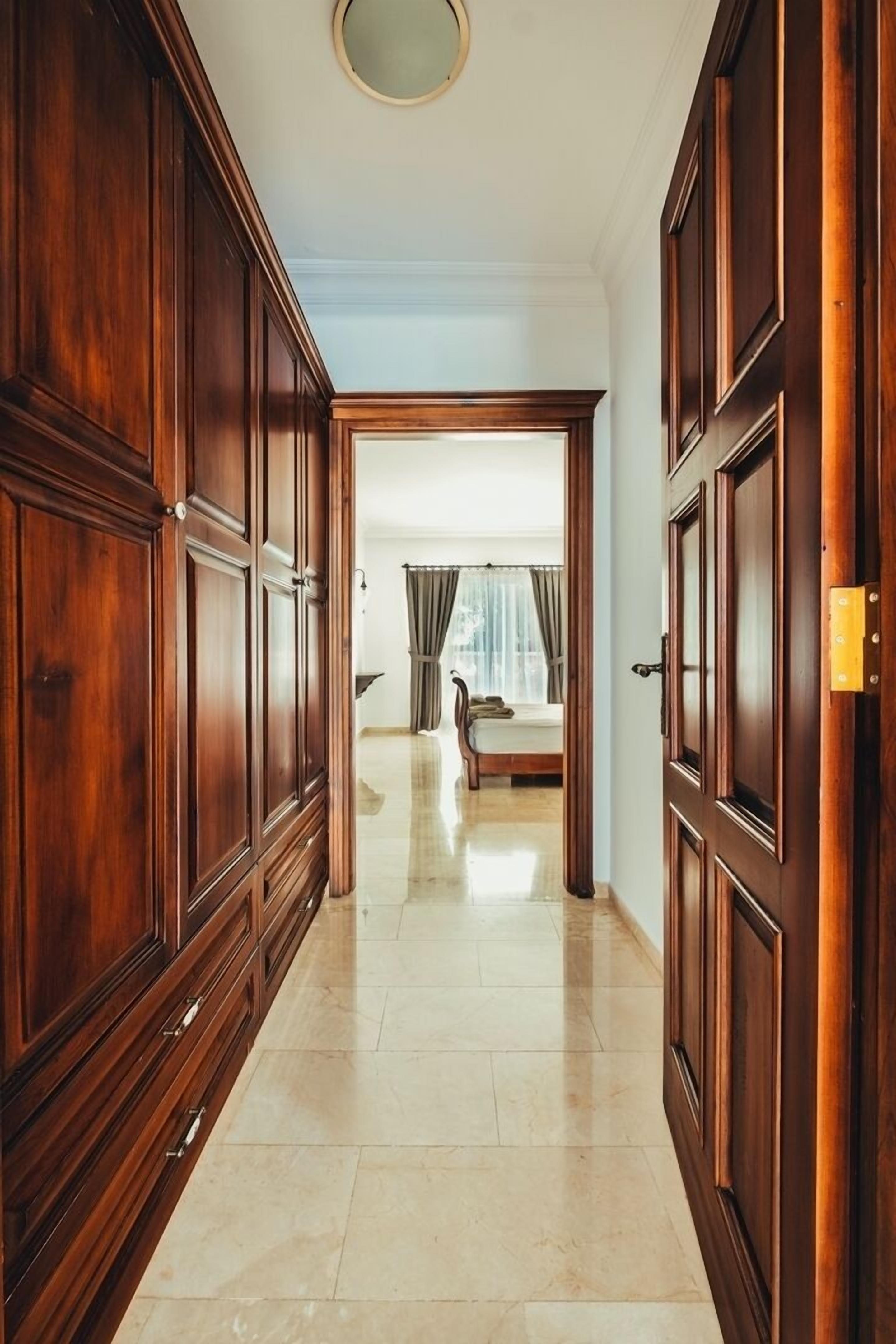 A hallway with wooden paneling and a bed in the background.