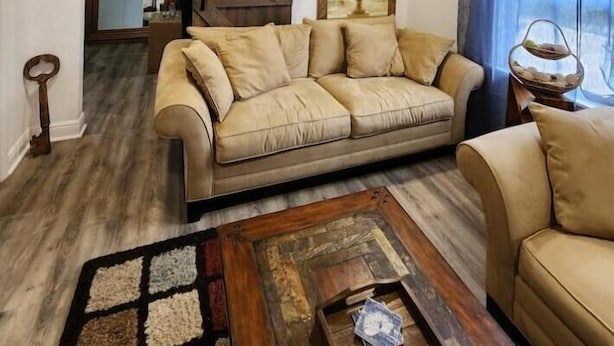 Un soggiorno con un divano beige, un tavolino in legno e un'ampia finestra con tende azzurre.