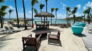 Un espace aménagé sur la plage avec des chaises longues, une table en bois et un parasol en chaume.