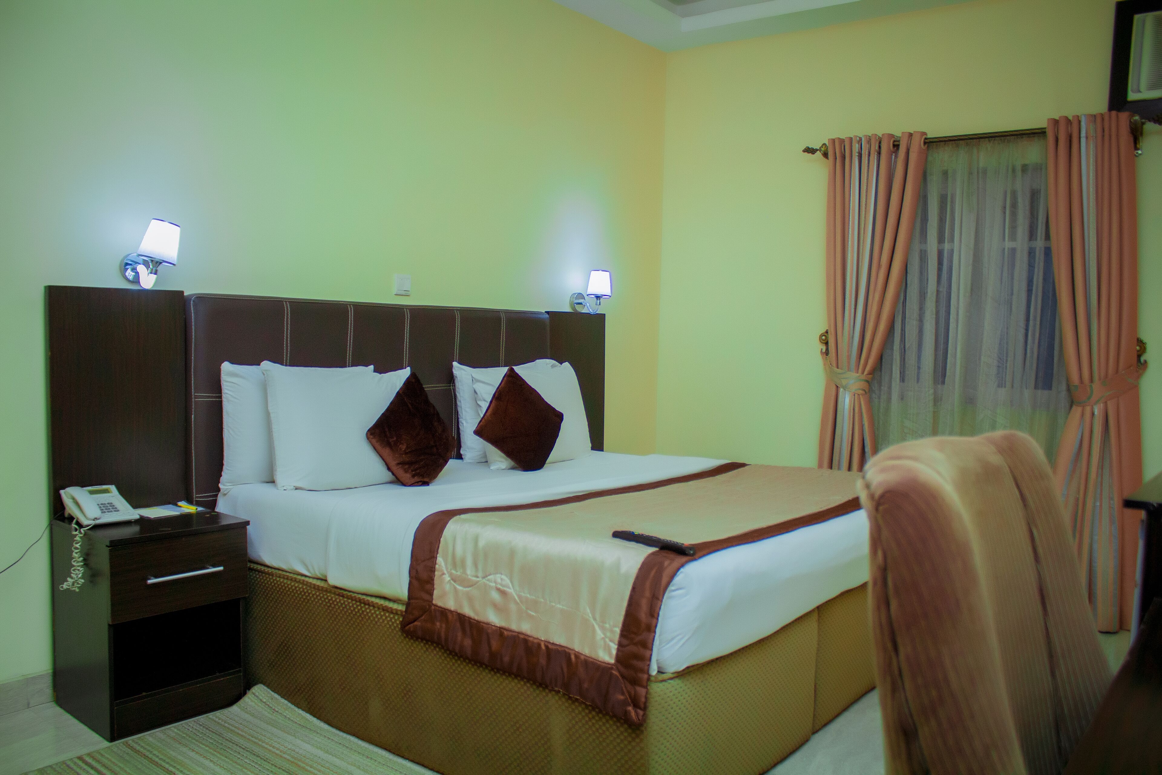 A hotel room with a bed, bedside tables, lamps, a window with curtains, and a chair.