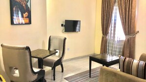 A living room with a dining table, two chairs, a sofa, a TV mounted on the wall, and a window with curtains. - Forever Hotels and Suites (Owerri)