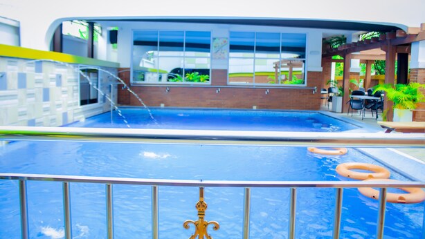 An indoor swimming pool with clear glass walls, a metal railing, and a few orange swim rings. - Forever Hotels and Suites (Owerri)