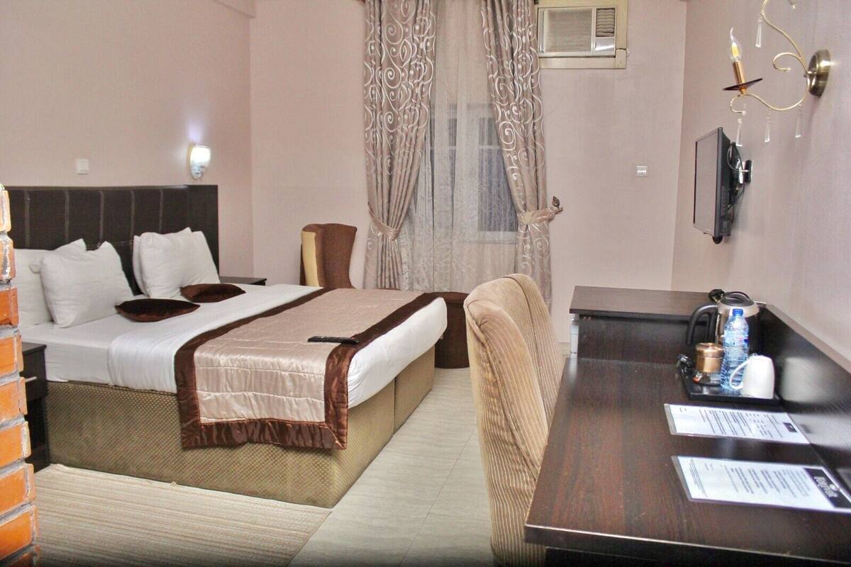 A hotel room with a bed, bedside table, chair, and a desk with a chair.