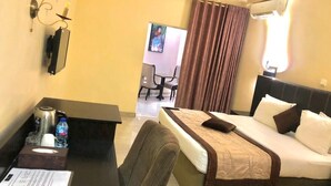 A hotel room with a bed, a desk with a chair, a small table, and a TV. - Forever Hotels and Suites (Owerri)