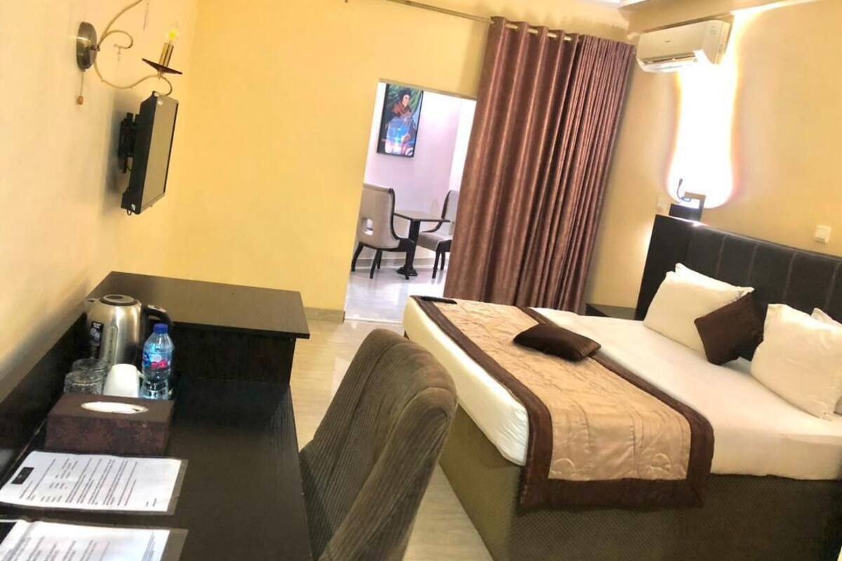 A hotel room with a bed, a desk with a chair, a small table, and a TV.