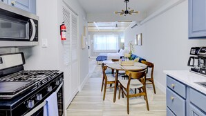 A compact kitchen with a stove, microwave, and coffee machine. A dining area with a table and chairs is visible in the background. - Modern Studio with King Bed, Free Parking & Wi-Fi (Memphis)