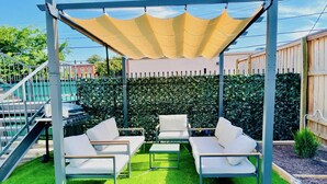 An outdoor patio with a pergola, white cushioned seating, and a green lawn. - Modern Studio with King Bed, Free Parking & Wi-Fi (Memphis)