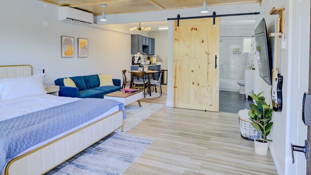 A modern bedroom with a large bed, a sofa, a dining area, and a sliding door to a bathroom. - Modern Studio with King Bed, Free Parking & Wi-Fi (Memphis)