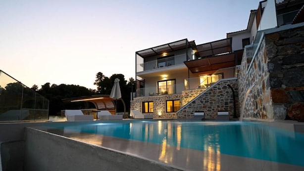 A modern two-story house with a swimming pool, stone walls, and a waterfall feature. - Royal Villa 2 (Skiathos)