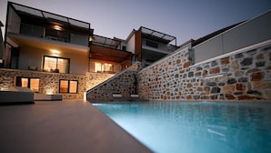 A modern poolside area with a stone wall and a two-story building with balconies. - Royal Villa 2 (Skiathos)
