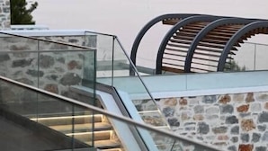 A modern staircase with glass railings leading to a terrace overlooking a body of water. - Royal Villa 2 (Skiathos)